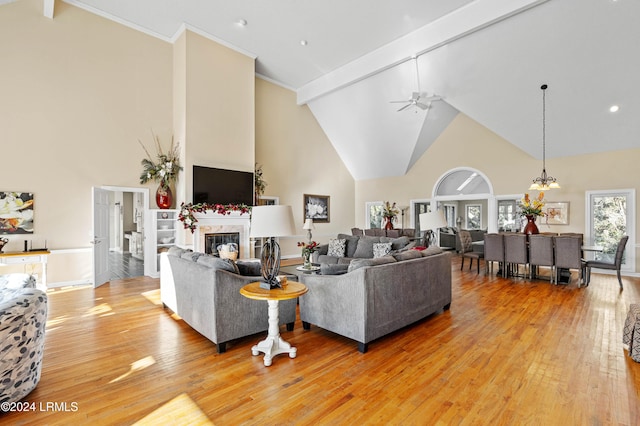 living room featuring beam ceiling, high vaulted ceiling, a high end fireplace, light hardwood / wood-style floors, and ceiling fan with notable chandelier