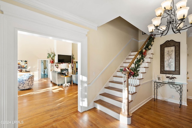 staircase with hardwood / wood-style floors, crown molding, and a chandelier