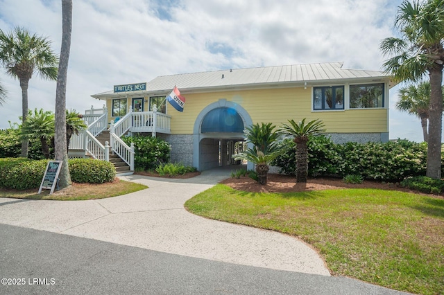 raised beach house with driveway, metal roof, stairway, and a front yard