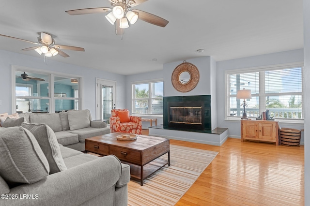 living room with ceiling fan, light wood finished floors, a glass covered fireplace, and baseboards