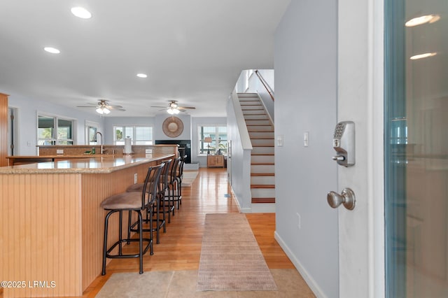 kitchen with a sink, a kitchen bar, a ceiling fan, recessed lighting, and light stone counters