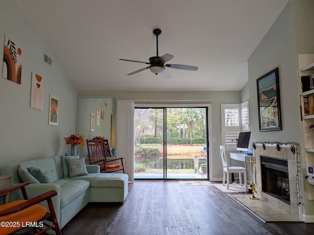 living room with wood-type flooring, a tile fireplace, ceiling fan, and vaulted ceiling