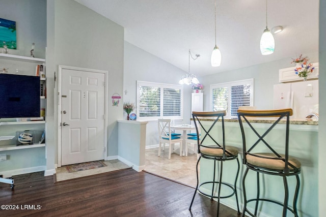 kitchen with a breakfast bar area, high vaulted ceiling, dark hardwood / wood-style floors, white fridge, and pendant lighting