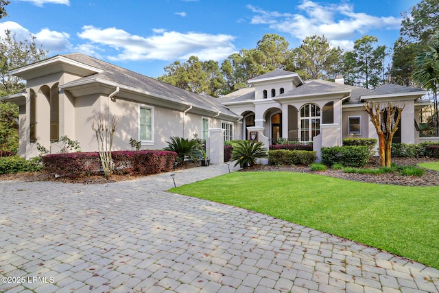 view of front of house with a front lawn, decorative driveway, a chimney, and stucco siding