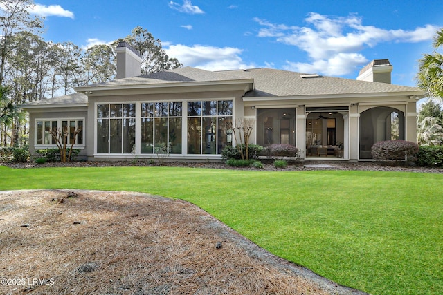 back of house featuring stucco siding, a chimney, a yard, and a sunroom