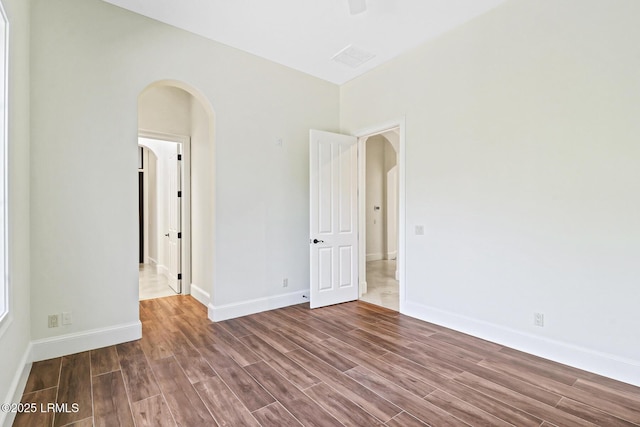 unfurnished room featuring wood finished floors, arched walkways, and baseboards