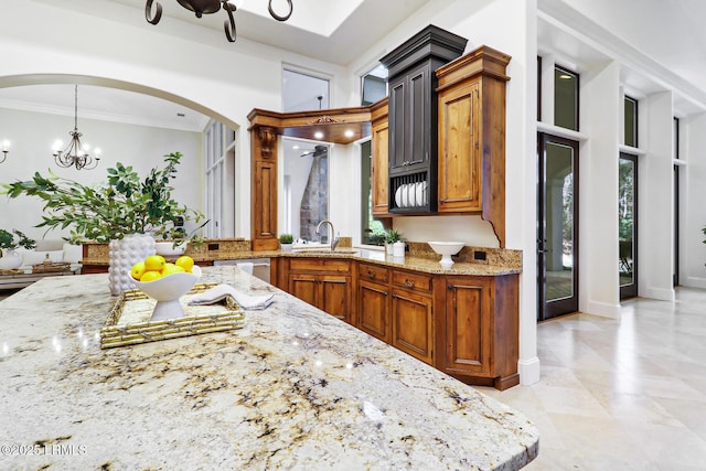 kitchen with a notable chandelier, light stone counters, a sink, arched walkways, and crown molding