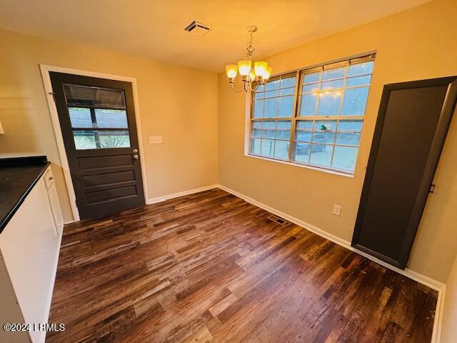 unfurnished dining area featuring an inviting chandelier and dark hardwood / wood-style floors