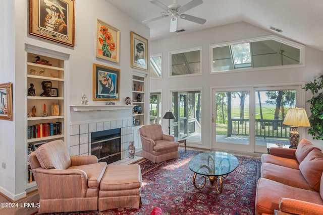 living room featuring built in shelves, ceiling fan, a tiled fireplace, and hardwood / wood-style flooring