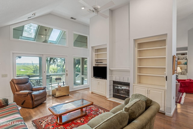 living room featuring high vaulted ceiling, a textured ceiling, built in features, a fireplace, and light hardwood / wood-style floors