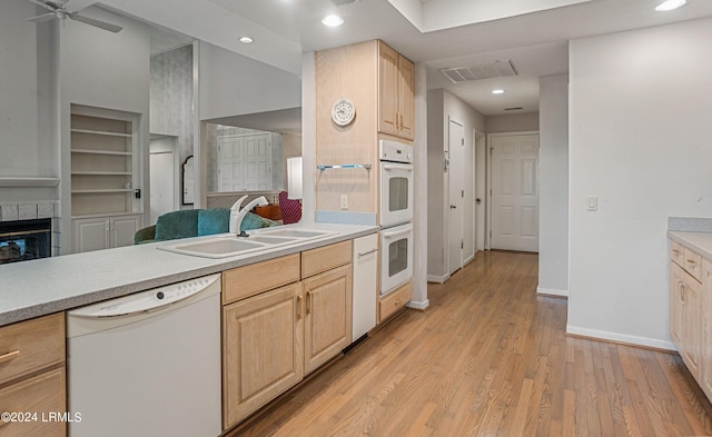 kitchen featuring built in shelves, light brown cabinetry, sink, white appliances, and a tiled fireplace