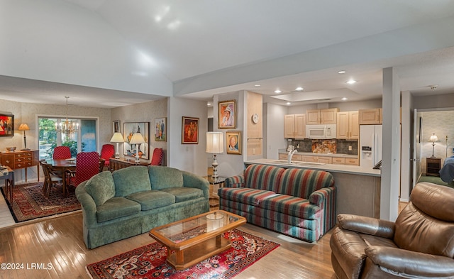 living room featuring lofted ceiling, sink, an inviting chandelier, and light wood-type flooring