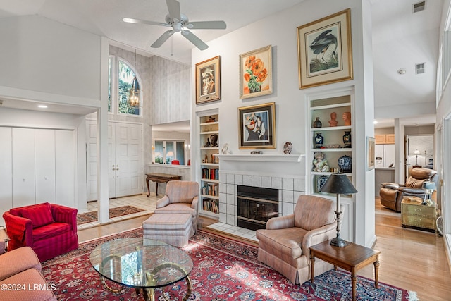 living room featuring a tiled fireplace, high vaulted ceiling, built in features, and light hardwood / wood-style flooring