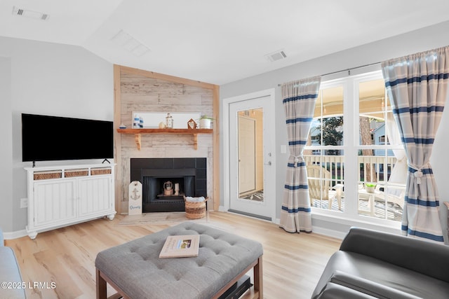 living room with a tiled fireplace, lofted ceiling, and light wood-type flooring