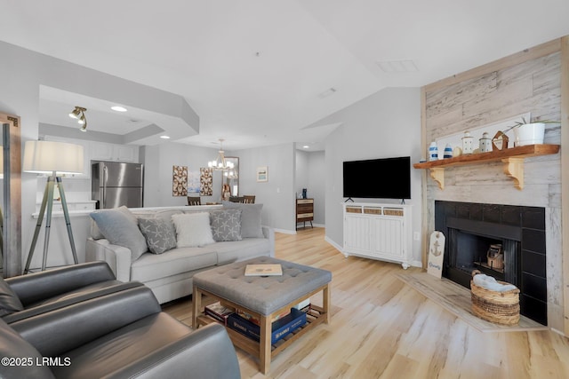 living room with vaulted ceiling, a notable chandelier, light hardwood / wood-style floors, and a fireplace