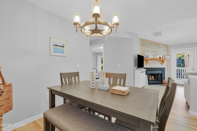 dining area with a healthy amount of sunlight, light wood-type flooring, a tile fireplace, and a notable chandelier