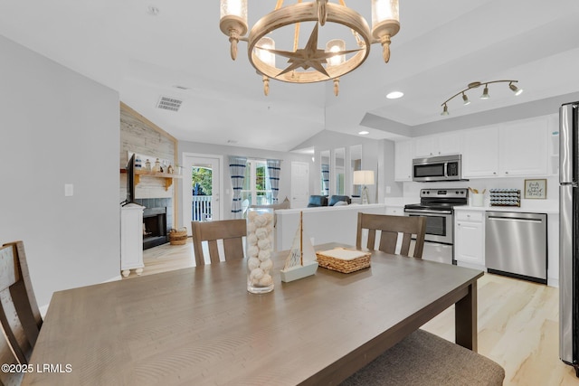 dining space with light hardwood / wood-style flooring, a tiled fireplace, vaulted ceiling, and a chandelier