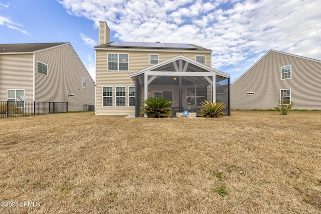 back of property featuring a yard, a sunroom, and solar panels