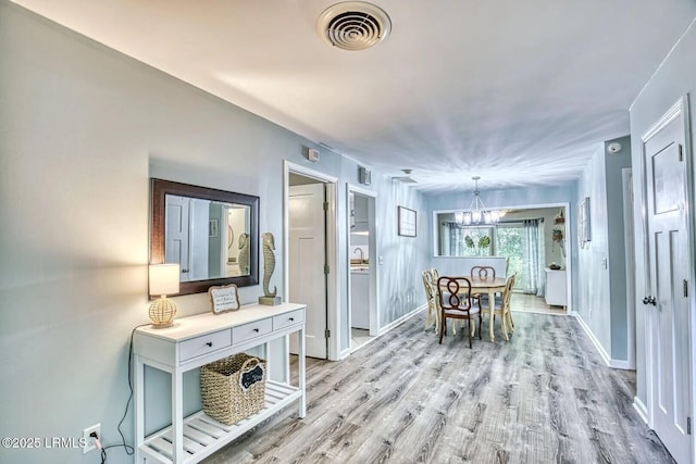 interior space featuring light wood-type flooring, visible vents, a notable chandelier, and baseboards