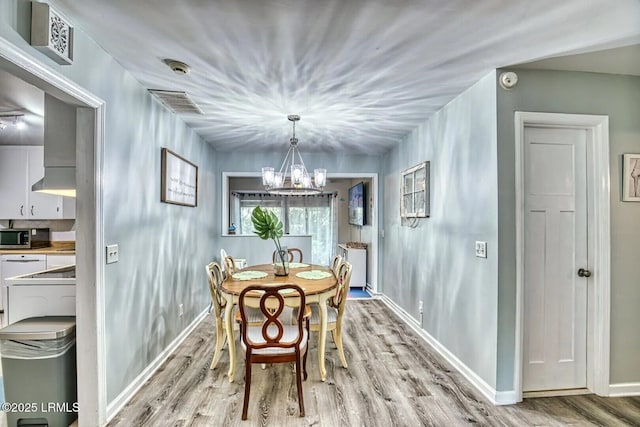 dining room with light wood finished floors, baseboards, visible vents, and a chandelier