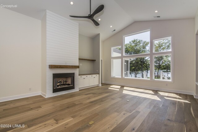 unfurnished living room with wood-type flooring, lofted ceiling, a large fireplace, and ceiling fan