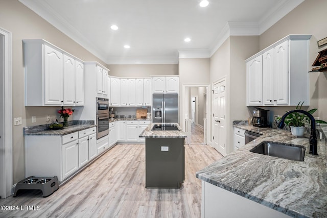 kitchen with sink, stainless steel appliances, white cabinets, a kitchen island, and dark stone counters