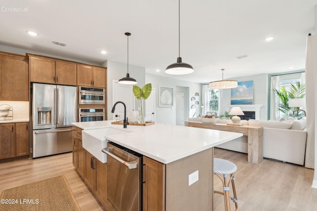 kitchen featuring appliances with stainless steel finishes, sink, a kitchen island with sink, and light hardwood / wood-style floors