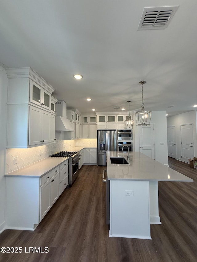 kitchen with a sink, visible vents, dark wood-style flooring, custom range hood, and appliances with stainless steel finishes