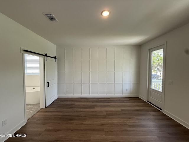 unfurnished room featuring dark wood finished floors, visible vents, a barn door, baseboards, and recessed lighting
