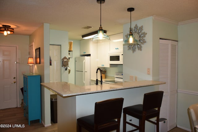 kitchen with pendant lighting, sink, a breakfast bar area, kitchen peninsula, and white appliances