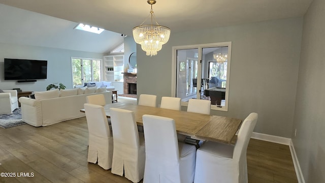 dining room with a brick fireplace, vaulted ceiling, wood finished floors, a chandelier, and baseboards