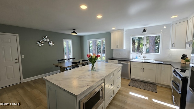 kitchen featuring white cabinets, dark countertops, appliances with stainless steel finishes, a center island, and a sink