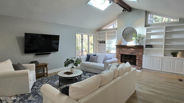 living area featuring a healthy amount of sunlight, a brick fireplace, light wood-style flooring, and beam ceiling
