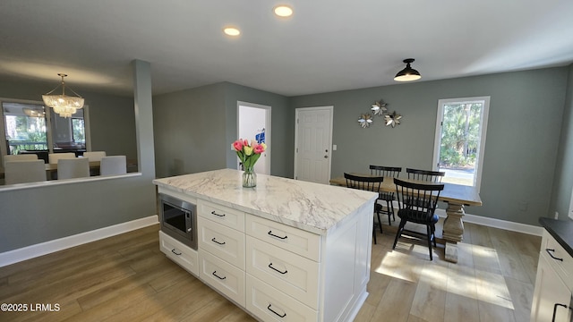 kitchen with a kitchen island, white cabinets, light wood-type flooring, stainless steel microwave, and pendant lighting