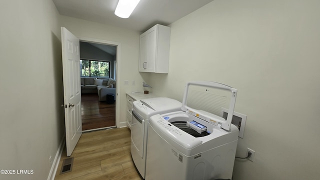 laundry room with cabinet space, visible vents, separate washer and dryer, light wood-type flooring, and baseboards