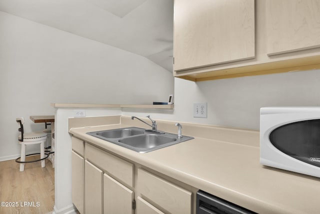 kitchen featuring lofted ceiling, light countertops, stainless steel dishwasher, light wood-style floors, and a sink