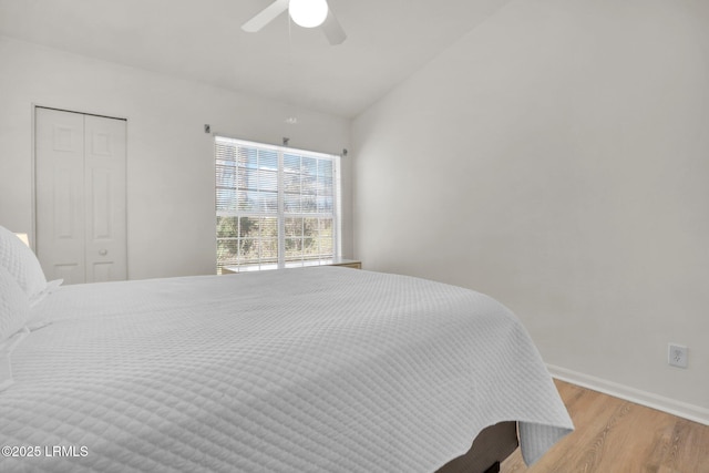 bedroom featuring ceiling fan, light wood-style flooring, baseboards, vaulted ceiling, and a closet