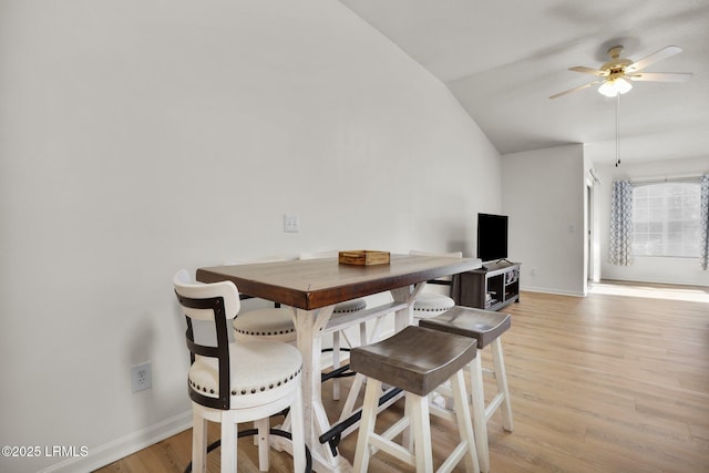 dining room featuring vaulted ceiling, ceiling fan, light wood-style flooring, and baseboards