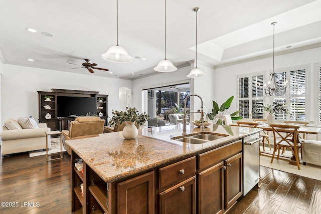 kitchen with light stone counters, a kitchen island with sink, sink, and pendant lighting