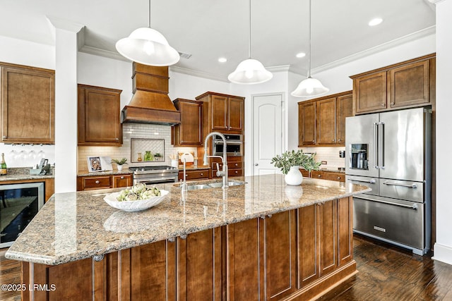 kitchen featuring pendant lighting, high quality appliances, an island with sink, sink, and wine cooler