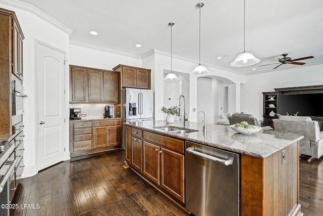 kitchen with appliances with stainless steel finishes, decorative light fixtures, sink, a kitchen island with sink, and light stone counters