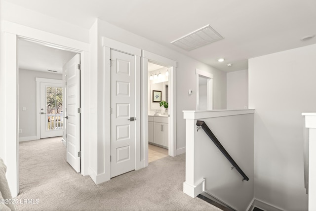 hall featuring visible vents, baseboards, an upstairs landing, and light colored carpet