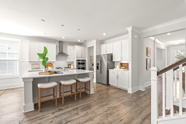 kitchen with a breakfast bar area, stainless steel appliances, backsplash, wall chimney exhaust hood, and an island with sink