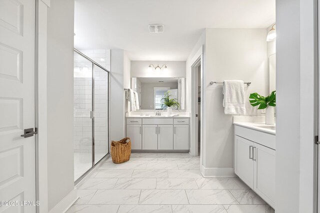 bathroom with a stall shower, baseboards, two vanities, marble finish floor, and a sink