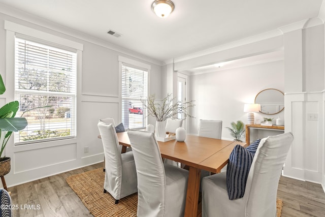 dining room featuring light wood-type flooring, visible vents, a decorative wall, and ornamental molding