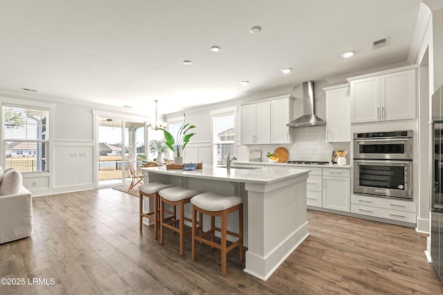 kitchen featuring double oven, gas cooktop, a sink, visible vents, and wall chimney exhaust hood