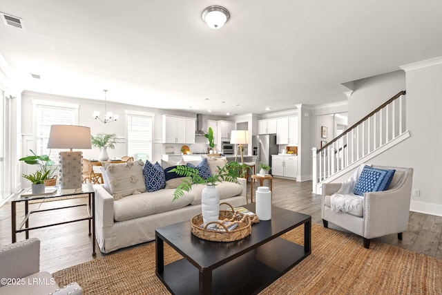 living area featuring visible vents, ornamental molding, wood finished floors, stairs, and a notable chandelier