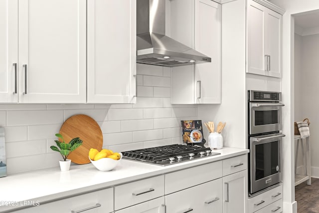 kitchen with wall chimney exhaust hood, appliances with stainless steel finishes, backsplash, and white cabinetry