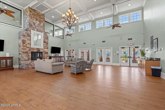 living room with light wood finished floors, baseboards, a ceiling fan, french doors, and a stone fireplace