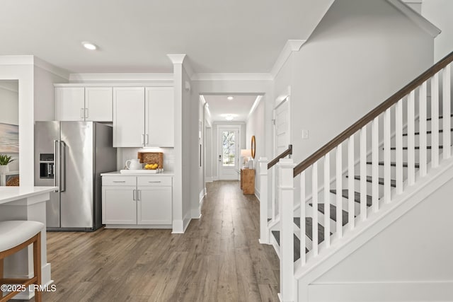 kitchen featuring high quality fridge, white cabinets, light wood-type flooring, backsplash, and crown molding